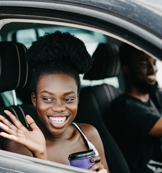 person smiling and waving out a car window